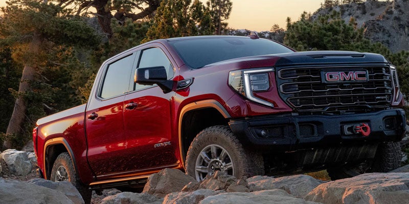 A red GMC Sierra 1500 parked on a rocky hill, showcasing its rugged design against a natural landscape.