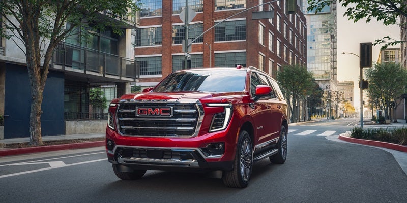 A GMC Yukon driving along a bustling city street, showcasing its sleek design and urban environment.